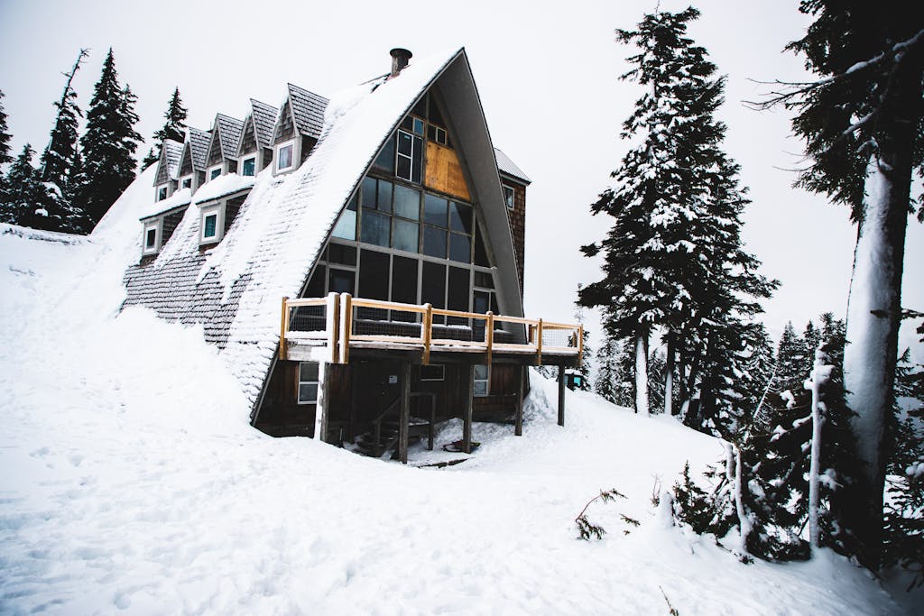 A picturesque snow-covered A-frame cabin surrounded by snowy trees in a winter landscape.